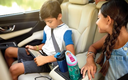 Two children in rear seats using the rear cup and bottle holders standard on the Subaru Ascent.